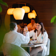 Ein Paar im Bademantel stößt beim Essen in der Sonne mit Wein an.